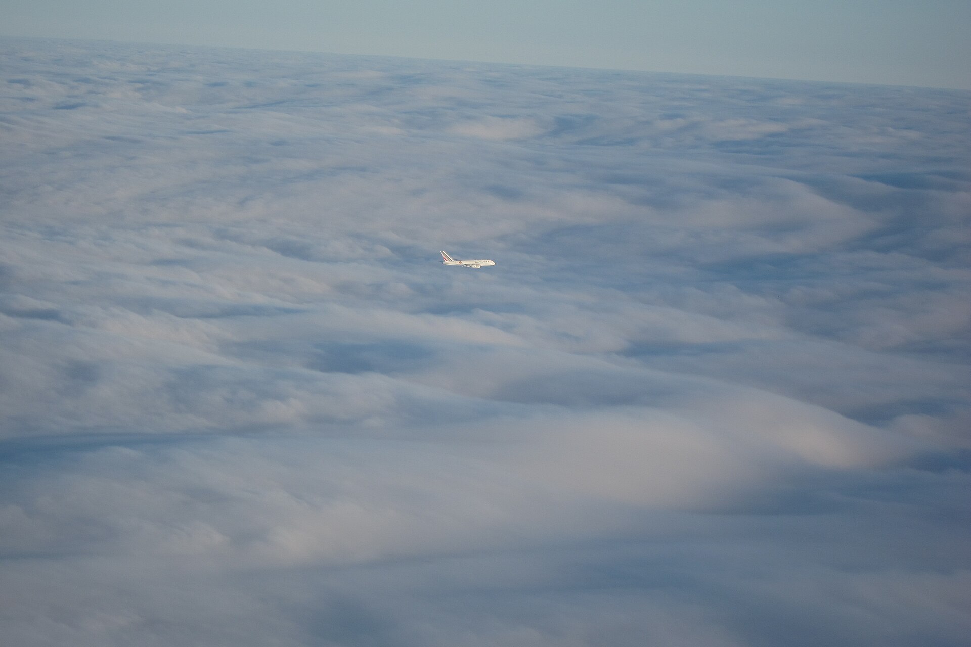 Vliegtuig vliegt hoog boven de wolken tegen een blauwe lucht
